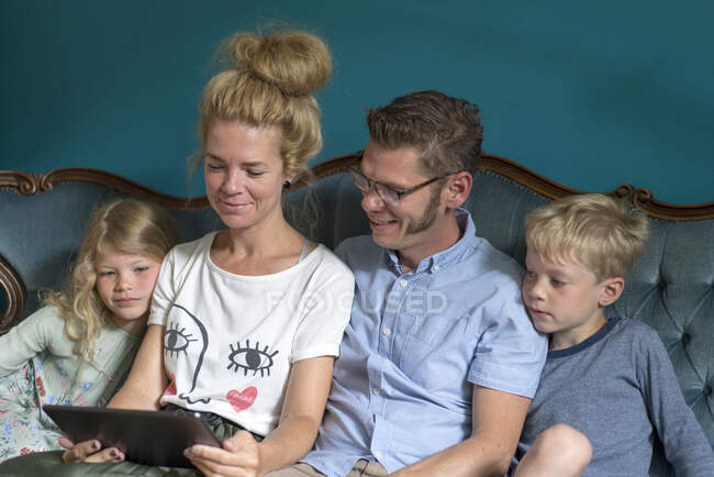 Семья делится цифровым планшетом, сидя дома на диване в гостиной — стоковое фото