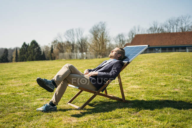 Бизнесмен отдыхает на стуле с солнечной панелью в парке в солнечный день — стоковое фото