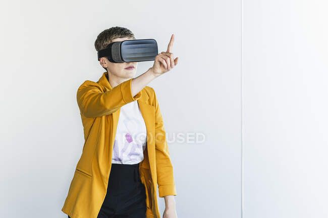 Businesswoman wearing blazer looking through virtual reality simulator while standing against wall in office — Photo de stock