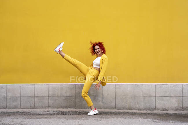 Energetic young woman in yellow suit running and jumping in front of yellow wall — Stock Photo