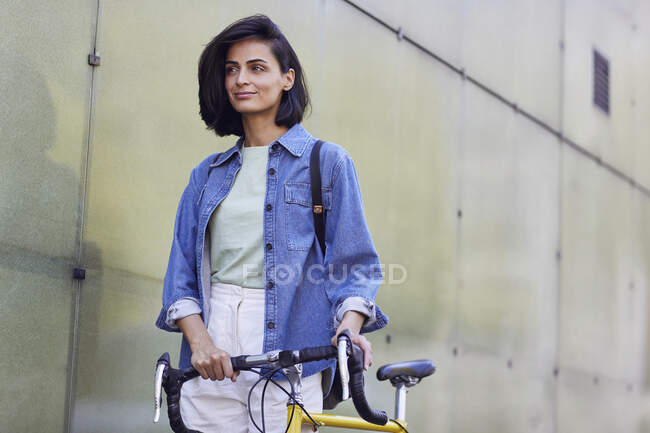 Comutador feminino cuidadoso com bicicleta em pé na parede da cidade — Fotografia de Stock