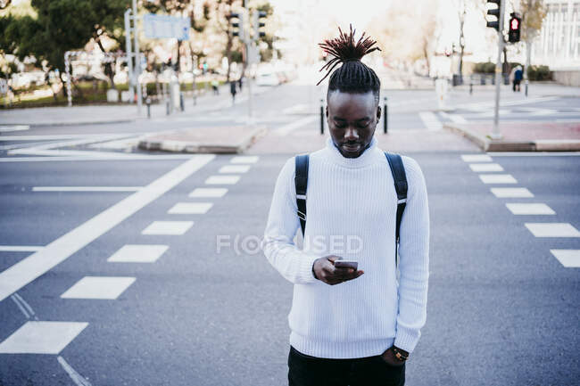 Giovane uomo d'affari creativo con le mani in tasca utilizzando il telefono cellulare sulla strada della città — Foto stock