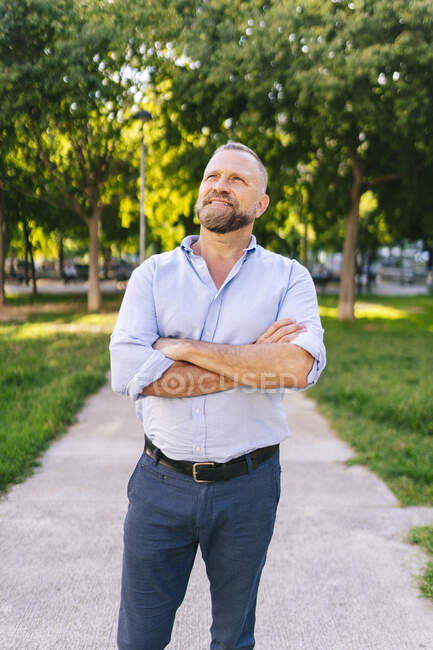 Uomo d'affari sorridente in piedi con le braccia incrociate al parco ufficio — Foto stock