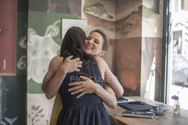 Souriante jeune femme d'affaires embrassant une amie dans un café — Photo de stock