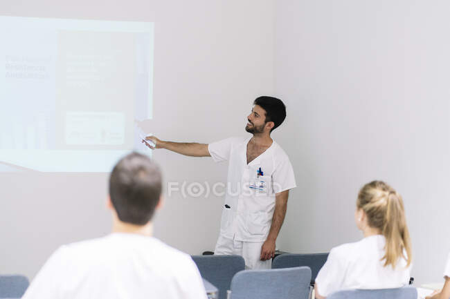 Medico di sesso maschile che spiega sopra lo schermo di proiezione ai colleghi in riunione in ospedale — Foto stock