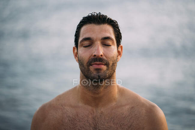 Primer plano del hombre guapo sin camisa con los ojos cerrados contra el mar - foto de stock