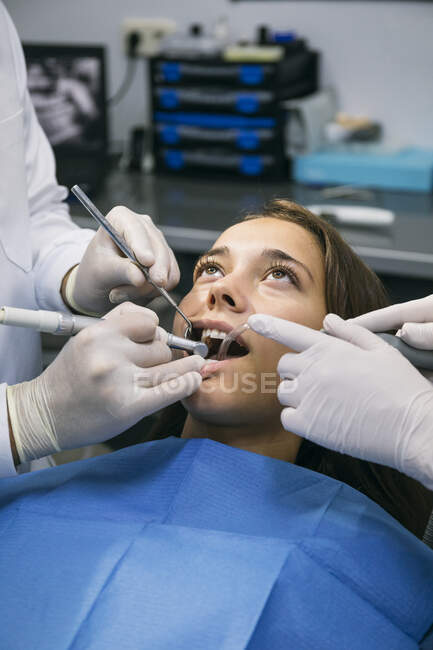 Dentista em luvas cirúrgicas fazendo tratamento dentário de paciente do sexo feminino com a ajuda de assistente na clínica — Fotografia de Stock