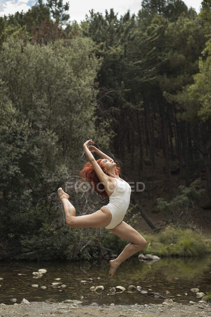 Mid adult woman practicing acrobatics at lakeshore in forest — Stock Photo