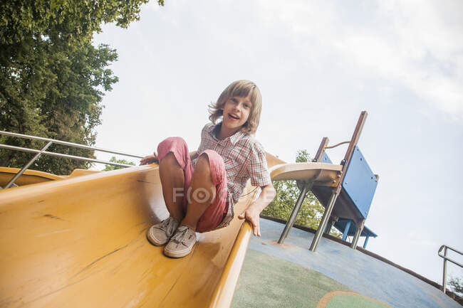 Niño jugando en la diapositiva contra el cielo en el parque - foto de stock