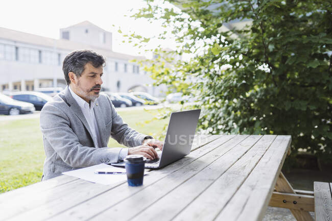 Homme d'affaires utilisant un ordinateur portable tout en travaillant à table contre un immeuble de bureaux — Photo de stock