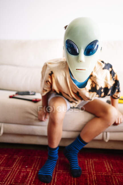Boy wearing alien mask sitting on sofa at home — Stock Photo