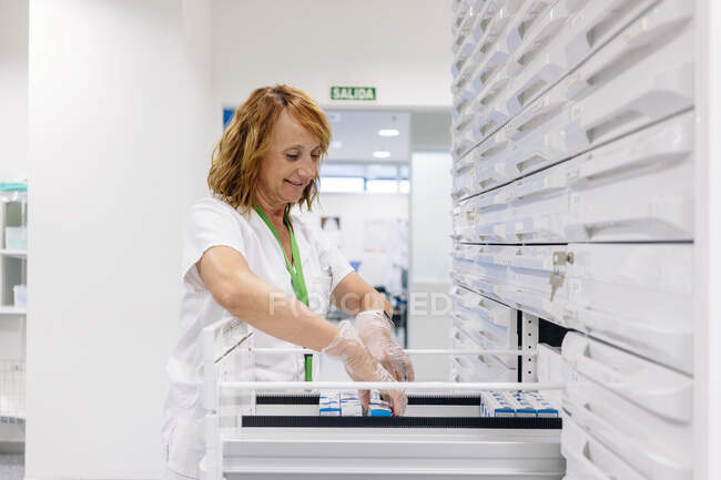 Farmacêutica feminina sorridente organizando medicamentos em gavetas no laboratório — Fotografia de Stock