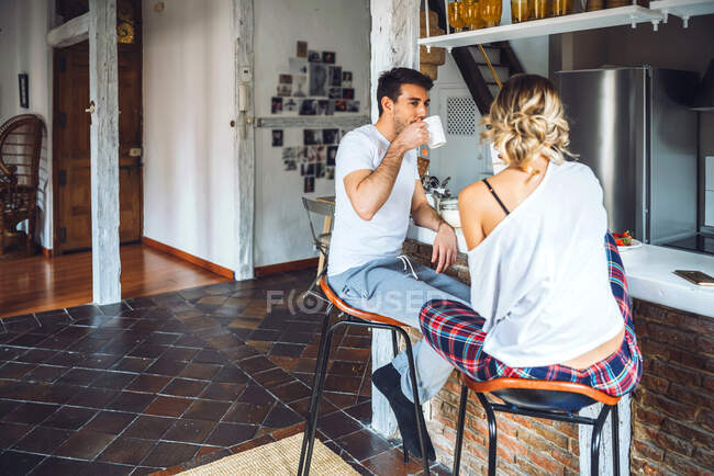 Young couple sitting at kitchen counter and having breakfast — Stock Photo