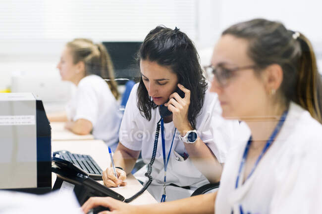 Farmacista donna che scrive mentre parla per telefono alla scrivania in ospedale — Foto stock