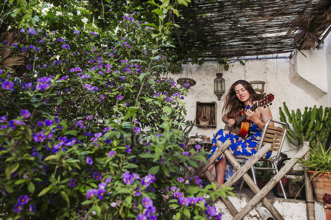 Young woman practicing guitar while sitting on chair in balcony — Stock Photo