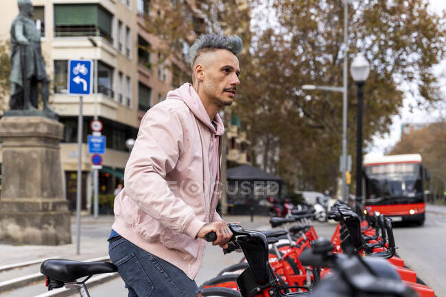 Stylish man looking away while renting bicycle at parking station — Stock Photo