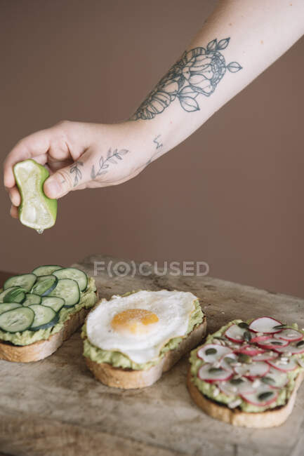 Жінка стискає лайм на хлібі, прикрашеному овочами та гуакамоле на страві на кухні — стокове фото