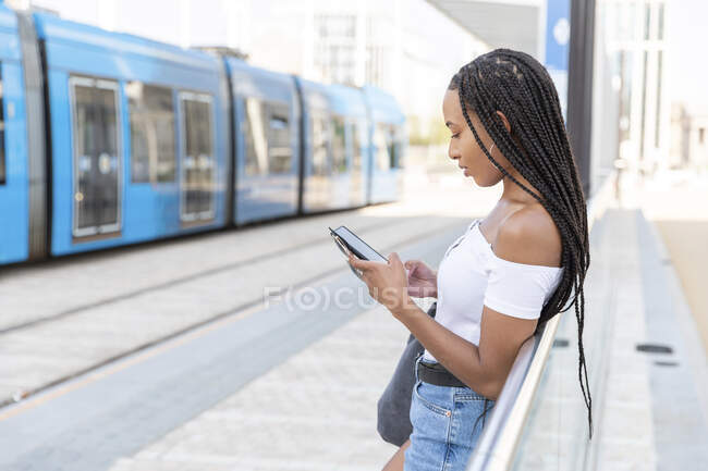 Молода жінка, використовуючи телефон, стоячи на залізничній станції — стокове фото