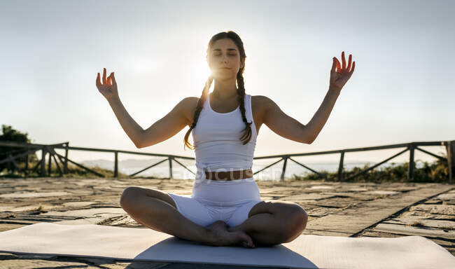 Junge Frau mit erhobenen Armen meditiert auf Matte vor klarem Himmel bei Sonnenuntergang — Stockfoto