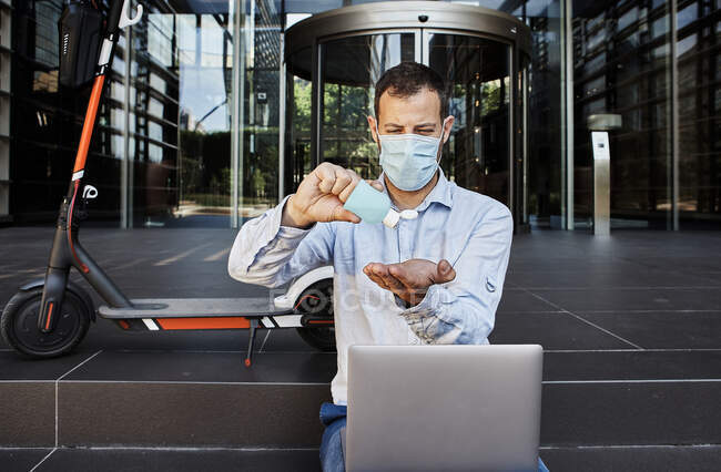 Entrepreneur with laptop sanitizing hands on staircase during coronavirus — Photo de stock