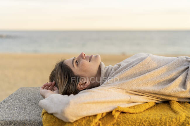 Junge Frau blickt bei Sonnenuntergang auf Bank an Strandpromenade auf — Stockfoto