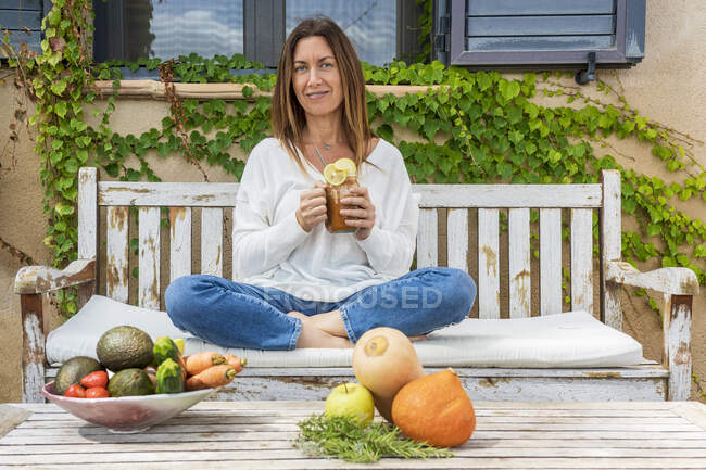 Mature female dietitian holding juice in jar while sitting with food at back yard — Stock Photo