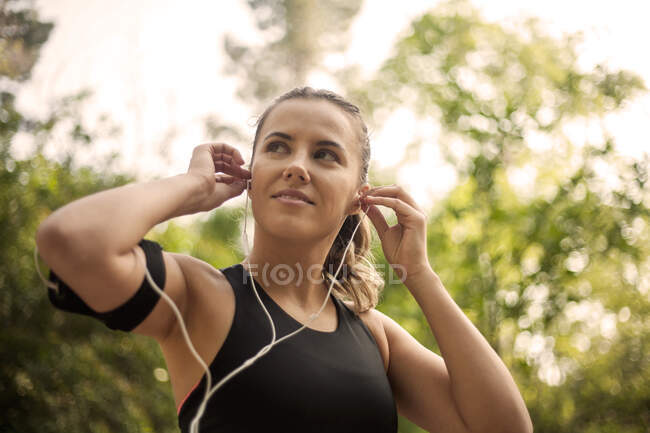 Sportlerin justiert Im-Ohr-Kopfhörer im Stehen — Stockfoto