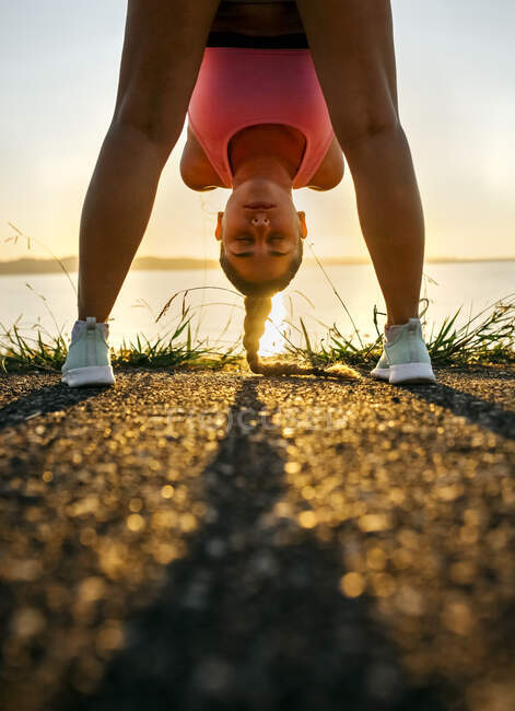 Young woman bending while exercising on road against sea at sunset — Stock Photo