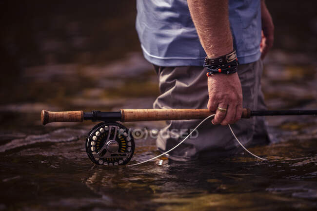 Close-up de mão de pescador segurando vara de pesca na mão enquanto está em pé no rio — Fotografia de Stock