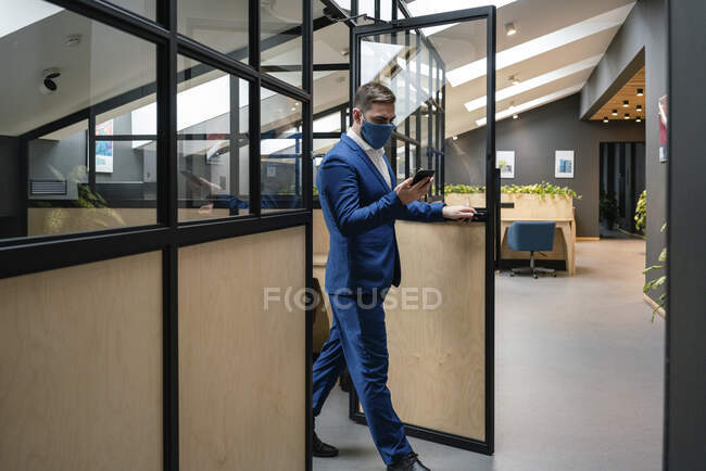 Businessman wearing protective face mask while walking out of cubicle at creative office during coronavirus pandemic — Foto stock