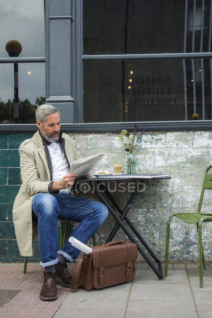 Mature businessman reading newspaper while sitting at sidewalk cafe — Stock Photo