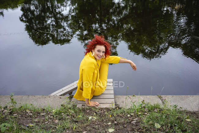 Young woman with curly hair and yellow suit sitting by the riverside — Foto stock