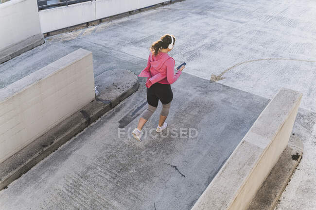 Юна жінка слухає музику й користується мобільним телефоном під час бігу на терасі. — стокове фото