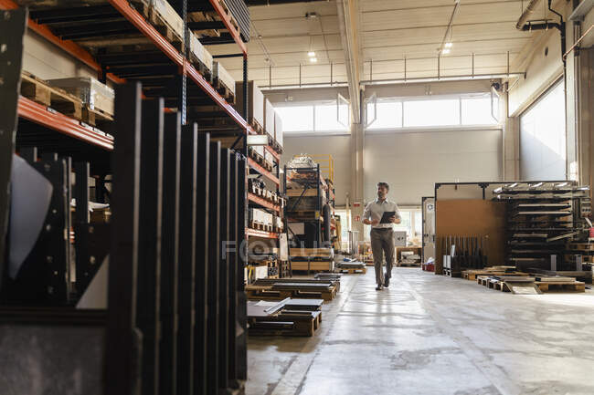 Homme d'affaires utilisant une tablette numérique tout en marchant à l'usine — Photo de stock