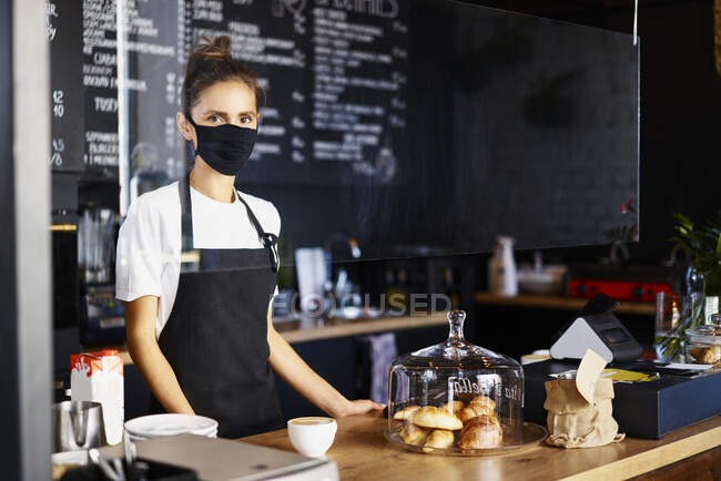 Retrato de camarera con mascarilla protectora mientras trabajaba en la cafetería - foto de stock