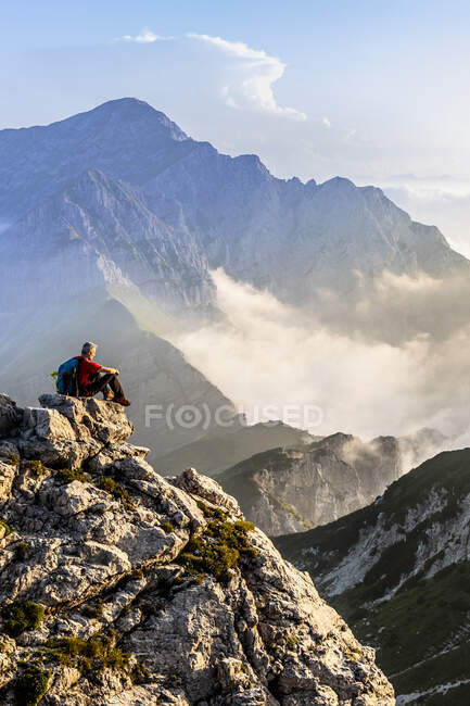 Excursionista admirando la vista mientras está sentado en el pico de la montaña en los Alpes bergamascos, Italia - foto de stock