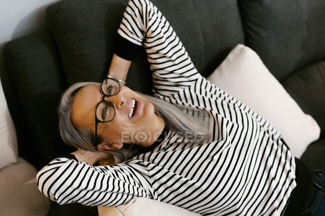 Donna spensierata seduta con le mani dietro la testa sul divano di casa — Foto stock