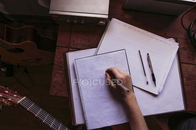Mujer joven escribiendo en libro en la mesa mientras practica la guitarra - foto de stock