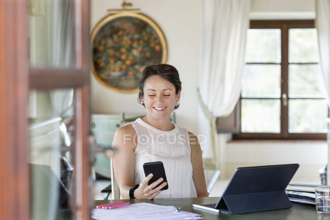 Усміхнена жінка-підприємець текстові повідомлення на смартфоні вдома — стокове фото