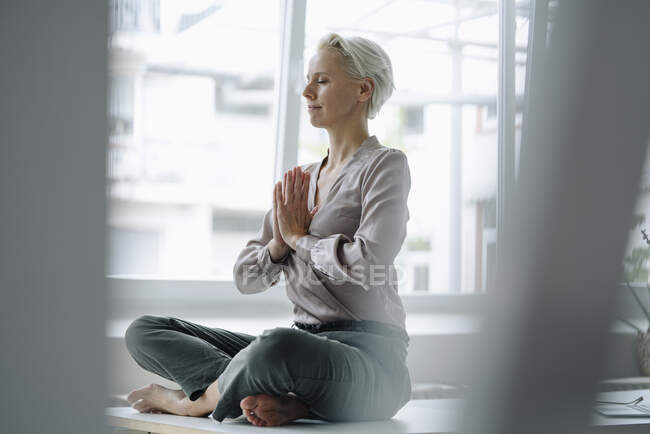 Зайнята жінка з закритими очима медитує, сидячи біля вікна в офісі — стокове фото