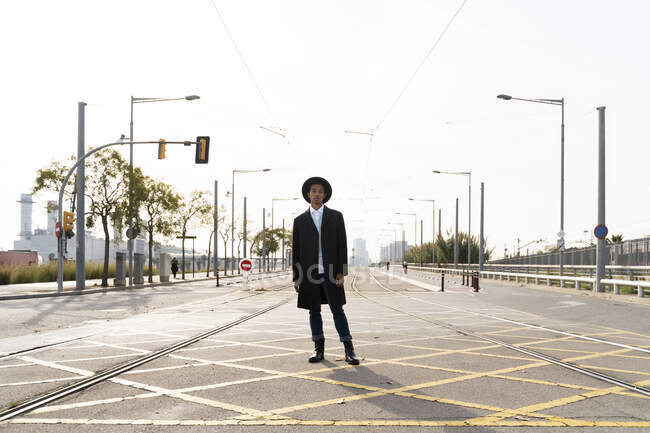 Junger Mann mit Hut steht bei sonnigem Wetter zwischen Bahngleisen auf der Straße — Stockfoto