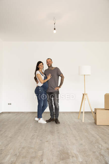 Coppia sorridente con lampada elettrica in piedi contro la parete nella nuova casa non arredata — Foto stock