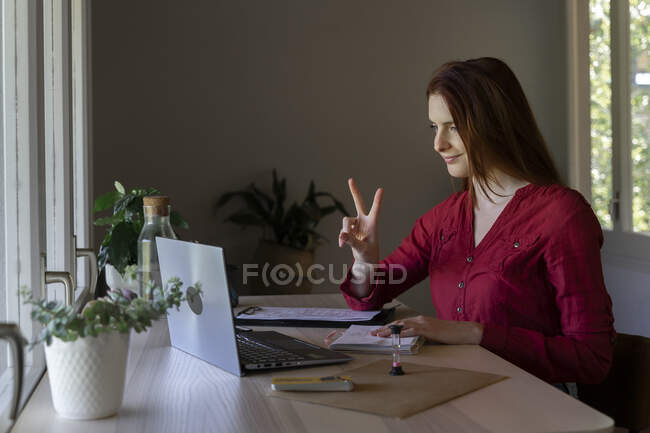 Доктор показує знак миру на відеодзвінку на ноутбуці, сидячи вдома. — стокове фото