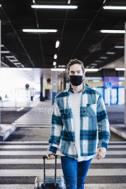 Молодой человек в маске для лица ходит с багажом по подземным дорогам — стоковое фото