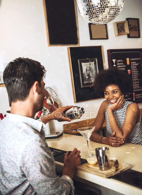 Усміхнена жінка дивиться на чоловічого бармена, який готує коктейль на стійці бару — стокове фото