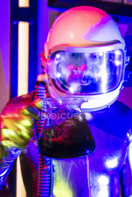 Gros plan d'un astronaute portant une combinaison spatiale tenant du café au sol dans une pièce éclairée — Photo de stock