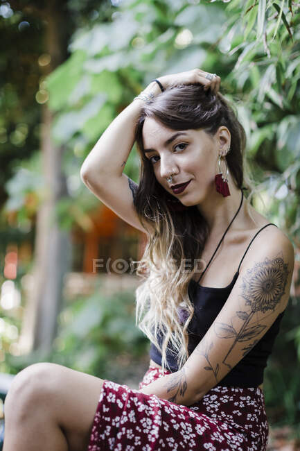 Frau mit Hand im Haar sitzt an Pflanze im Park — Stockfoto