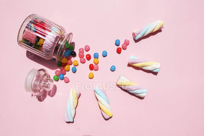 Captura de estudio de malvaviscos retorcidos y caramelos que salen del frasco derribado - foto de stock