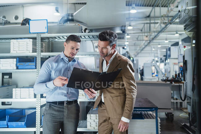 Empresário com colega de trabalho do sexo masculino discutindo sobre o documento de arquivo enquanto está na indústria — Fotografia de Stock