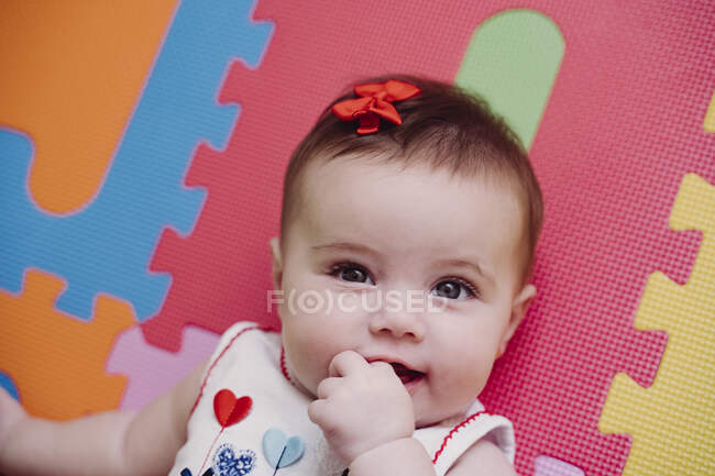 Close Up Portrait Of Cute Baby Girl With Finger In Mouth Lying On Puzzle Playmat At Home Colour Indoors Stock Photo